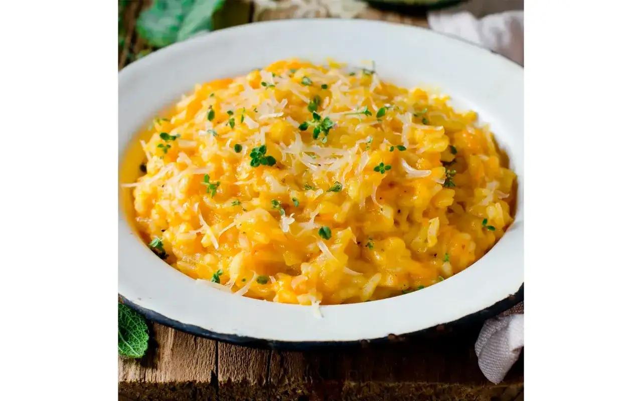 Risotto cremoso colorato con risotto zafferano in polvere, guarnito con parmigiano grattugiato e erbe aromatiche fresche.