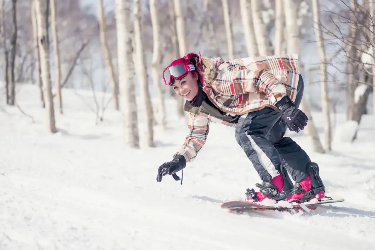Kobieta z różowymi włosami szusuje na snowboardzie po ośnieżonym stoku. Widok na polskie góry zimą.