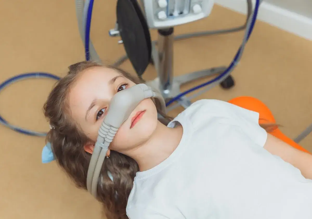 Dziewczynka z maską do sedacji u dentysty. Urządzenie medyczne zapewnia komfort podczas zabiegu.