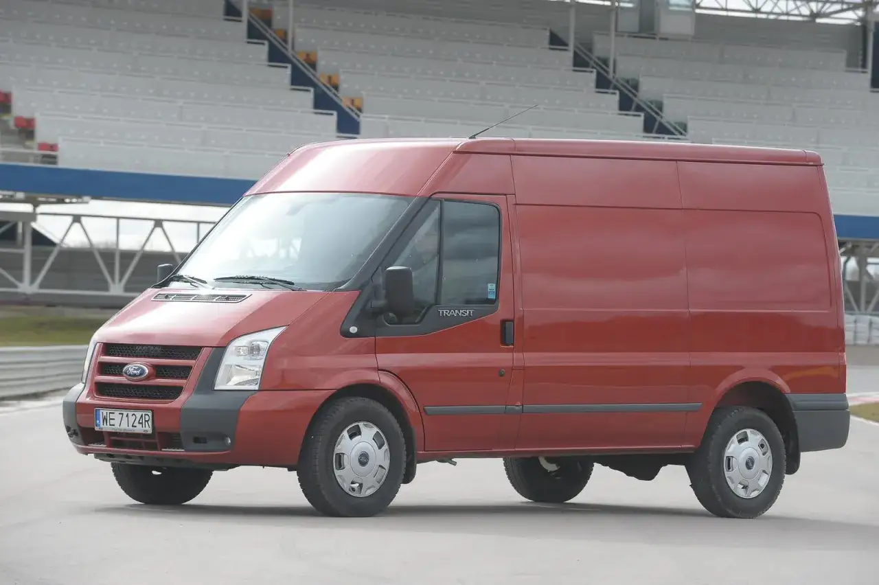 Czerwony Ford Transit 2018, gotowy do wymiany żarówki, stoi na torze wyścigowym.