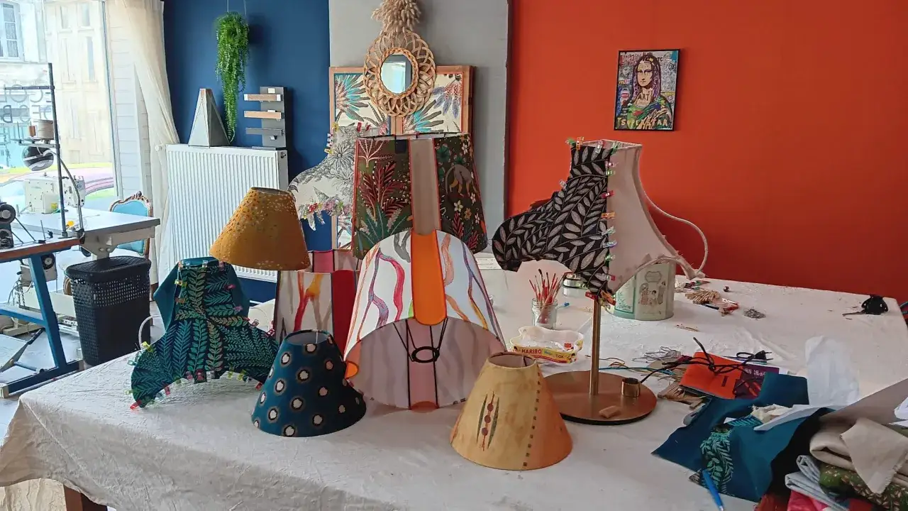 Atelier de création d'abat jour DIY. Divers abat-jour aux motifs variés, tissus, fils et matériel de couture sur une table.