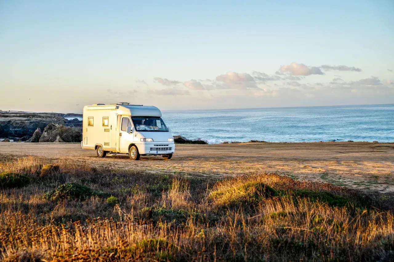 Autocaravana blanca en la costa, disfrutando de un viaje nacional 2 Portugal. El mar azul y el cielo despejado crean un paisaje id&iacute;lico.