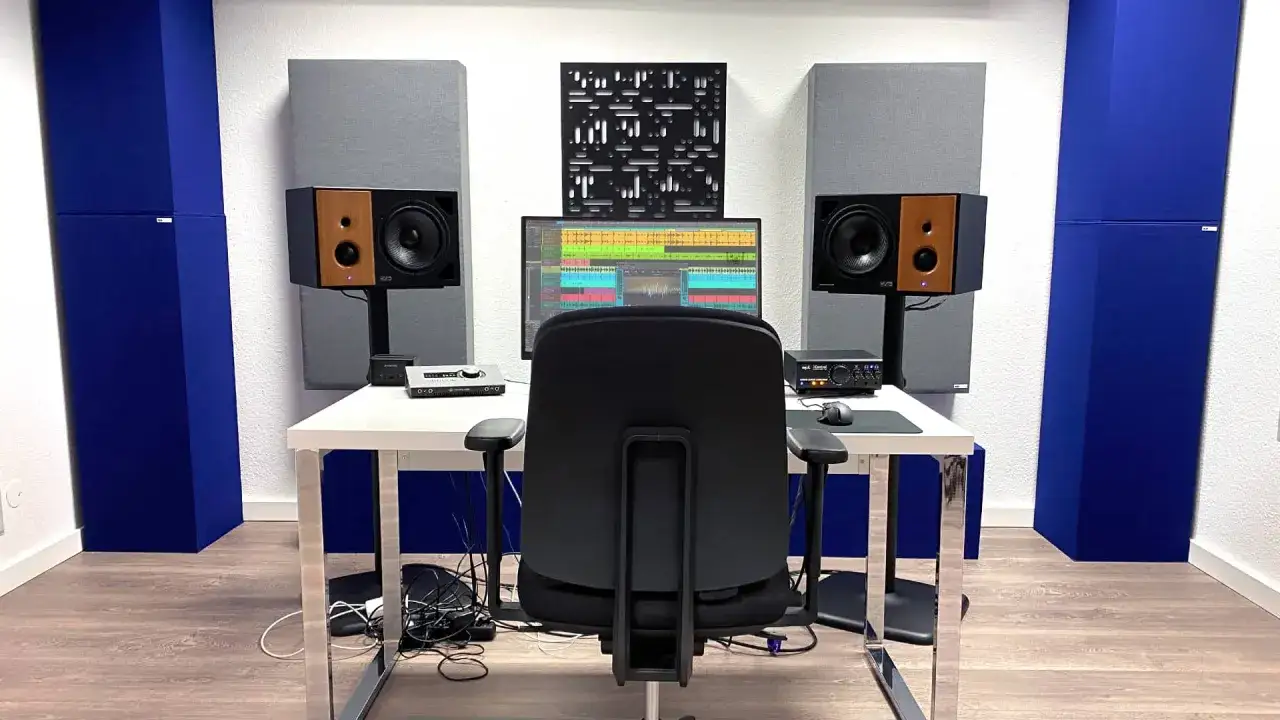 Studio-Setup mit Akustikpaneelen in Blau und Grau, um die **Akustik im Raum verbessern**. Ein Schreibtisch mit Monitor, Lautsprechern und einem Stuhl.