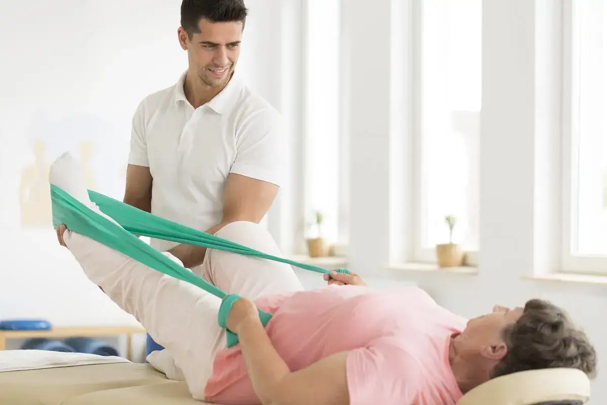 Fizjoterapeuta pomaga pacjentce po operacji biodra w ćwiczeniach z gumą rehabilitacyjną.