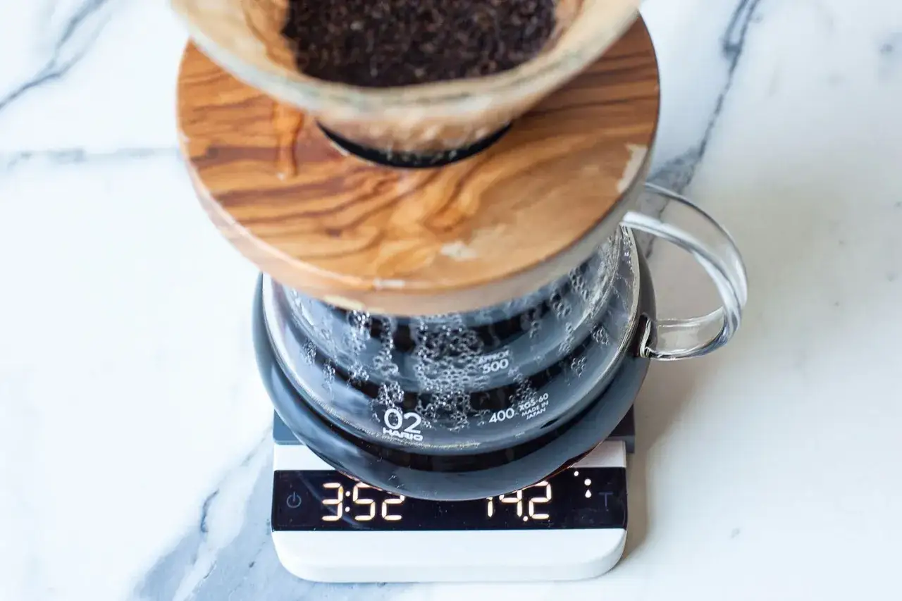 Kaffebryggning med V60. Kaffebryggaren står på en våg som visar tid och vikt, vilket indikerar noggrann kaffe dosering.