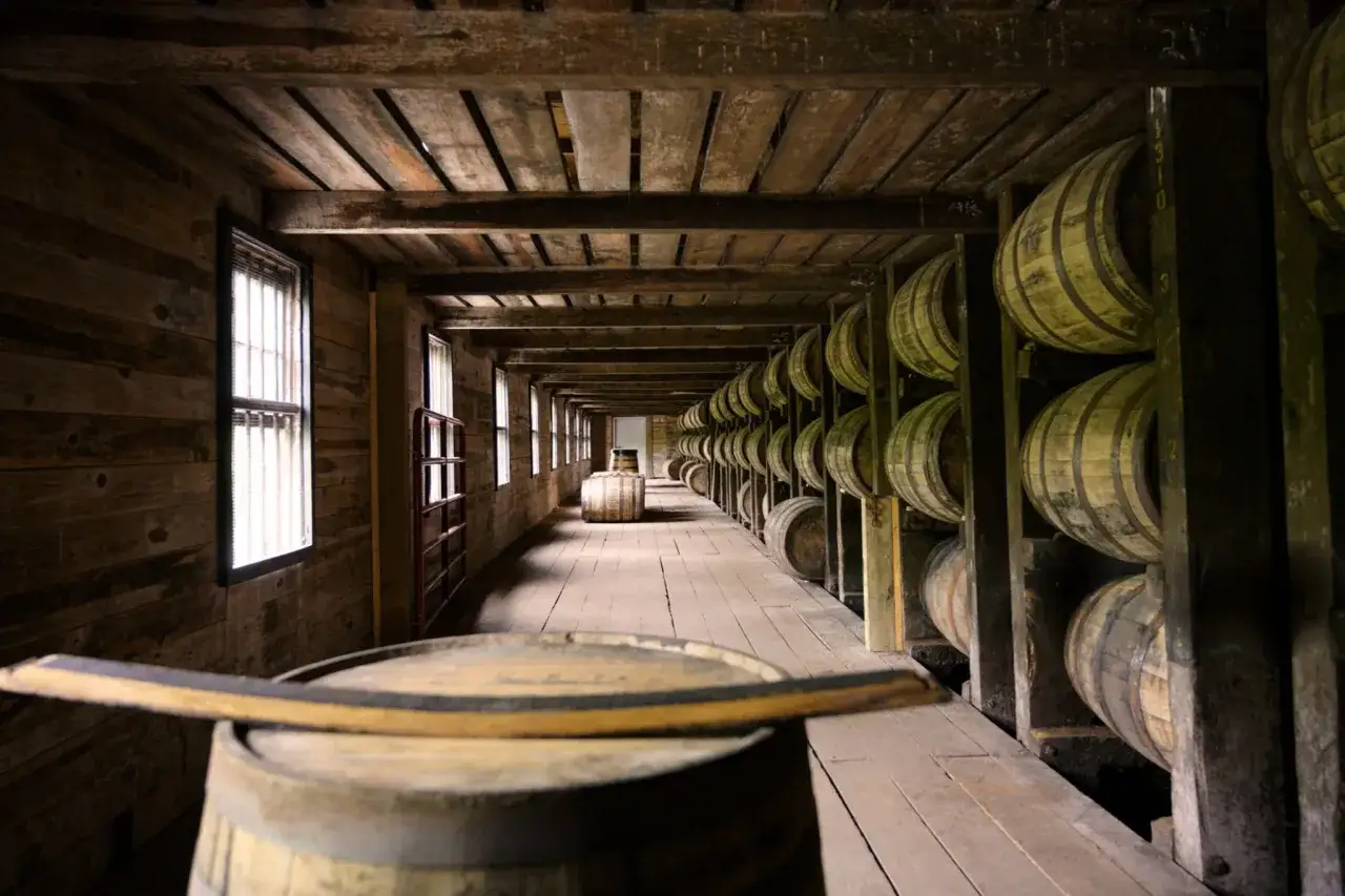 Allée sombre d'un chai en bois, remplie de fûts empilés. Un fût de bourbon est au premier plan, prêt à vieillir.