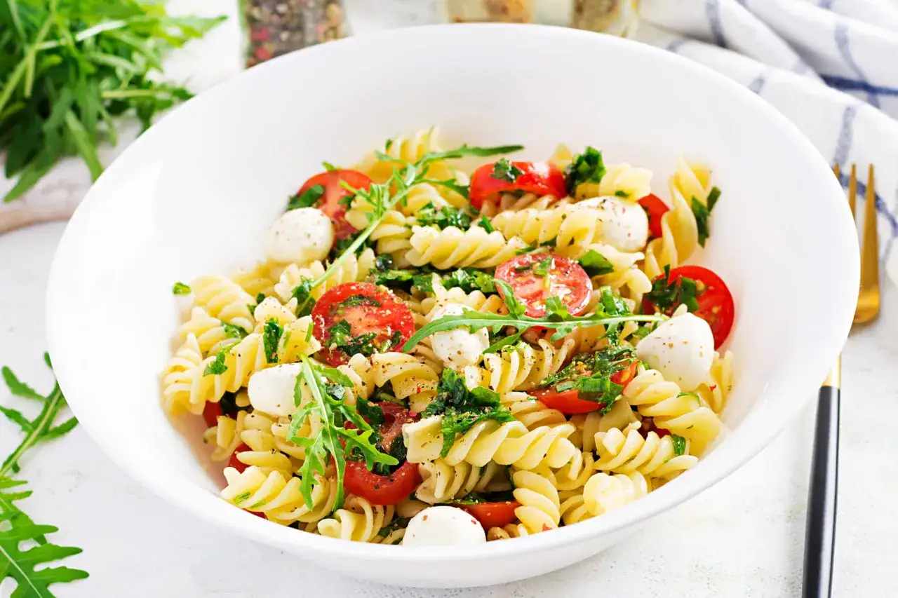 Ein k&ouml;stlicher Spaghetti-Salat mit Kirschtomaten, Mozzarella-Kugeln und Rucola, garniert mit Kr&auml;utern und Gew&uuml;rzen.