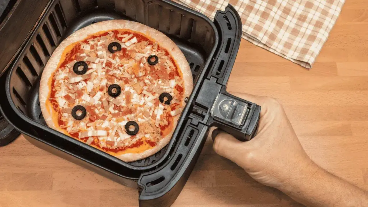 Une pizza garnie d'olives noires et de fromage est pr&ecirc;te &agrave; &ecirc;tre cuite dans un airfryer.