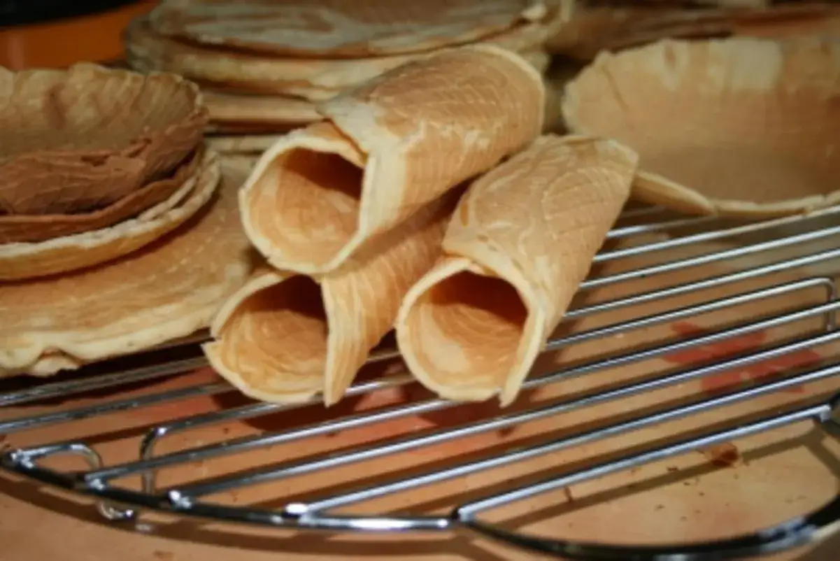 Omas Neujahrskuchen Rezept: Frisch gebackene, goldbraune Kekse in Röllchenform und flache Waffeln liegen auf einem Gitter.
