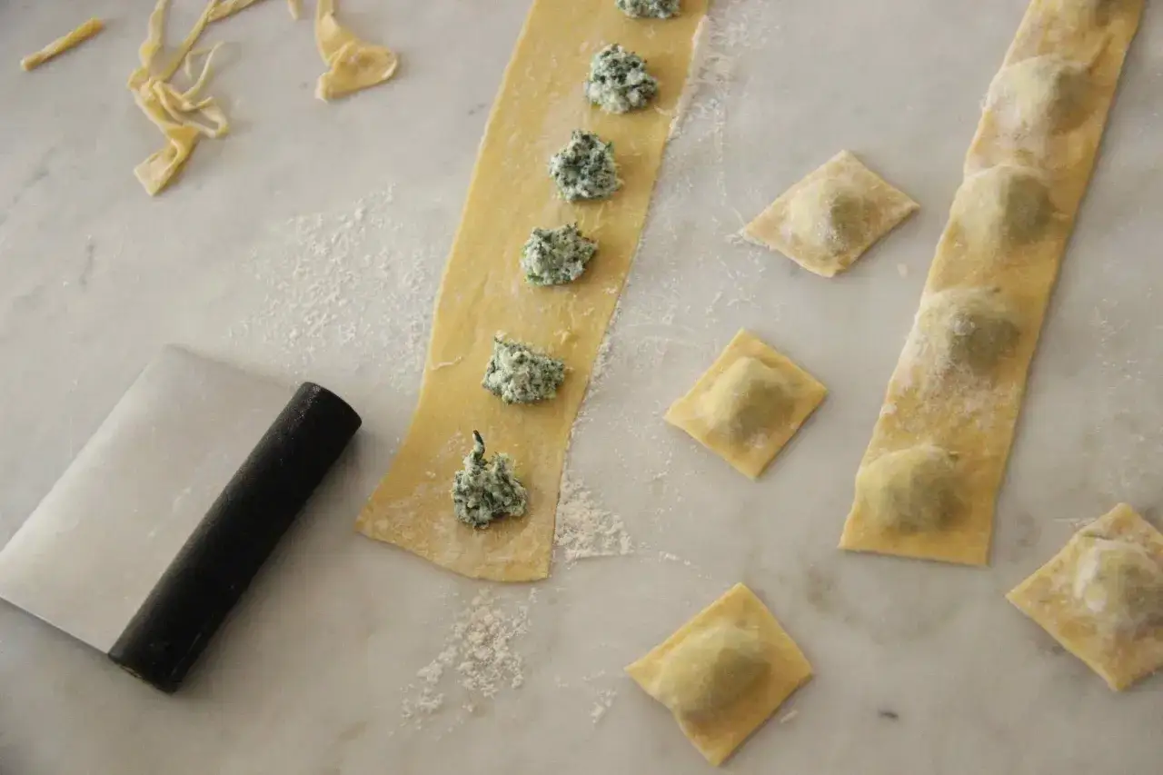 Pr&eacute;paration d'une recette de ravioli maison : p&acirc;te fra&icirc;che, farce verte et quelques raviolis d&eacute;j&agrave; form&eacute;s.