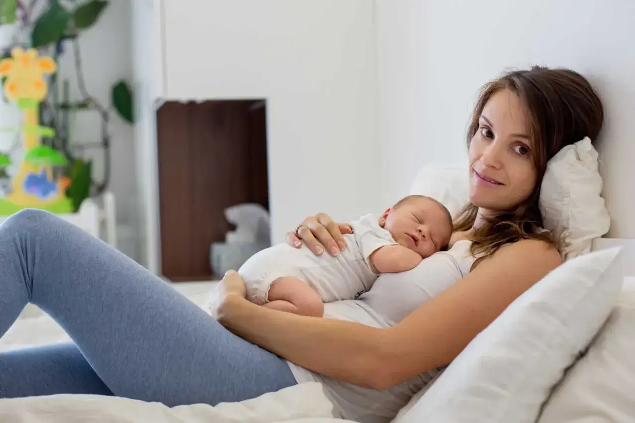 Mutter h&auml;lt schlafendes Baby im Arm. Trotz anf&auml;nglichem **Schwangerschaftsblues** strahlt sie Gl&uuml;ck aus.