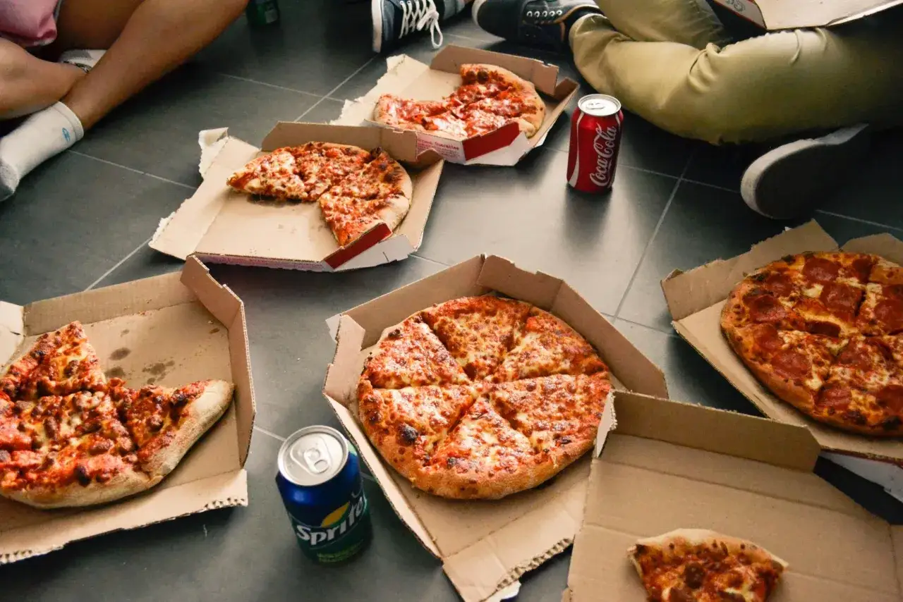 Kilka pizz w kartonach i puszki napojów na podłodze. Czy pizza jest zdrowa? To zależy od dodatków i sposobu przygotowania, ale dziś to idealna przekąska na spotkanie ze znajomymi.