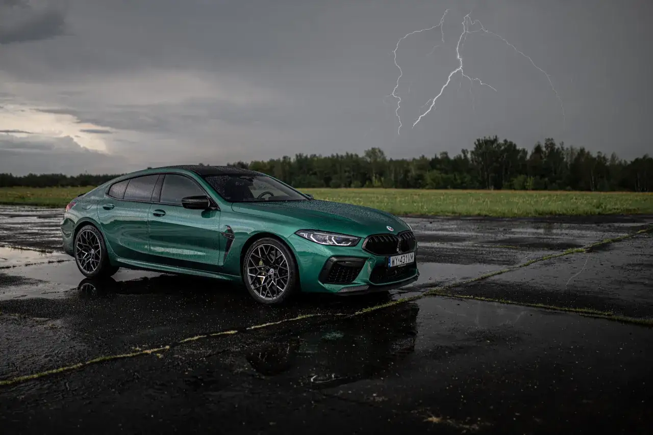 Zielone BMW M8 na mokrym asfalcie, z błyskawicą na burzowym niebie. Sprawdź, jaka jest aktualna bmw m8 cena.