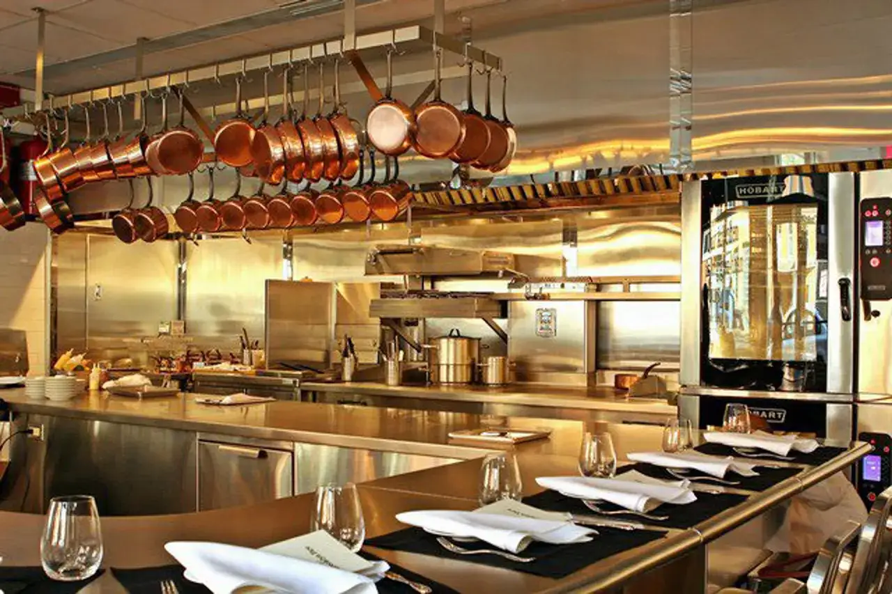Cocina profesional con ollas de cobre colgadas. Mesas puestas sugieren la experiencia que significan las estrellas Michelin.
