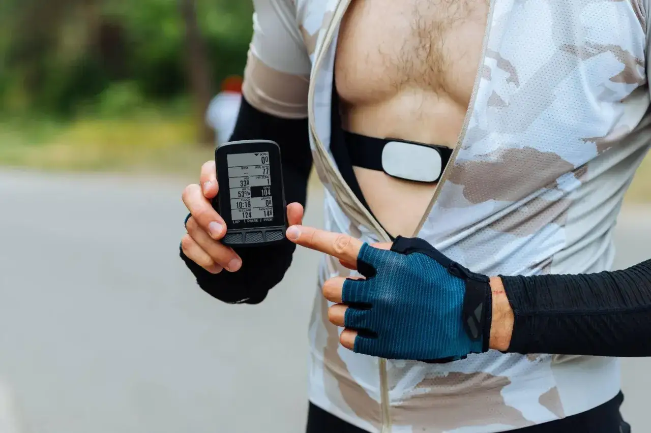 Cyclist checks heart rate monitor, aiming for zone 3 cycling. The device shows RPM, HR, and speed data.