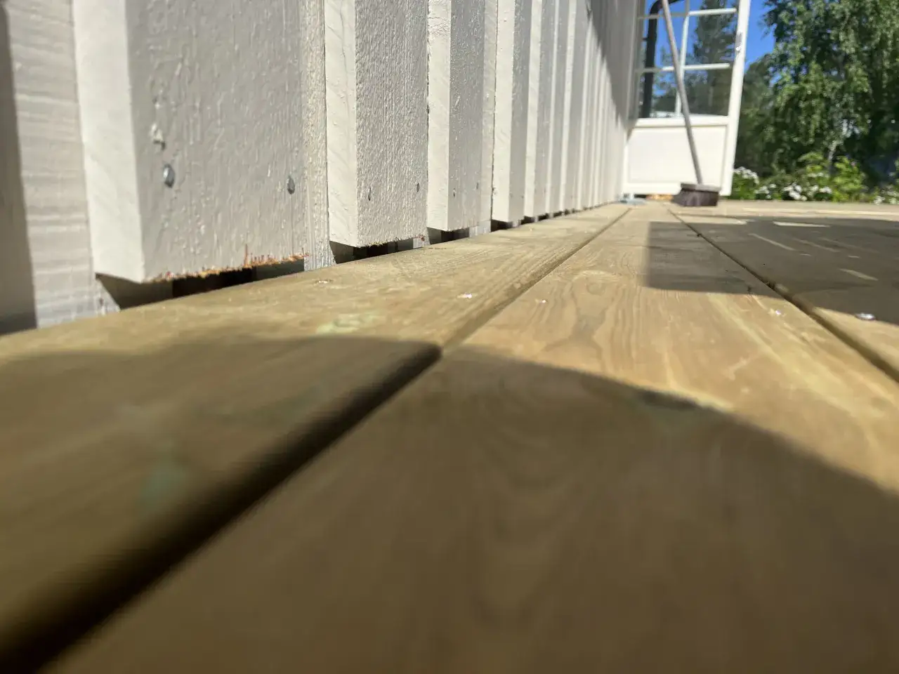 Nybyggd altan med en vitm&aring;lad plank st&aring;ende panel som reser sig mot en bl&aring; himmel.