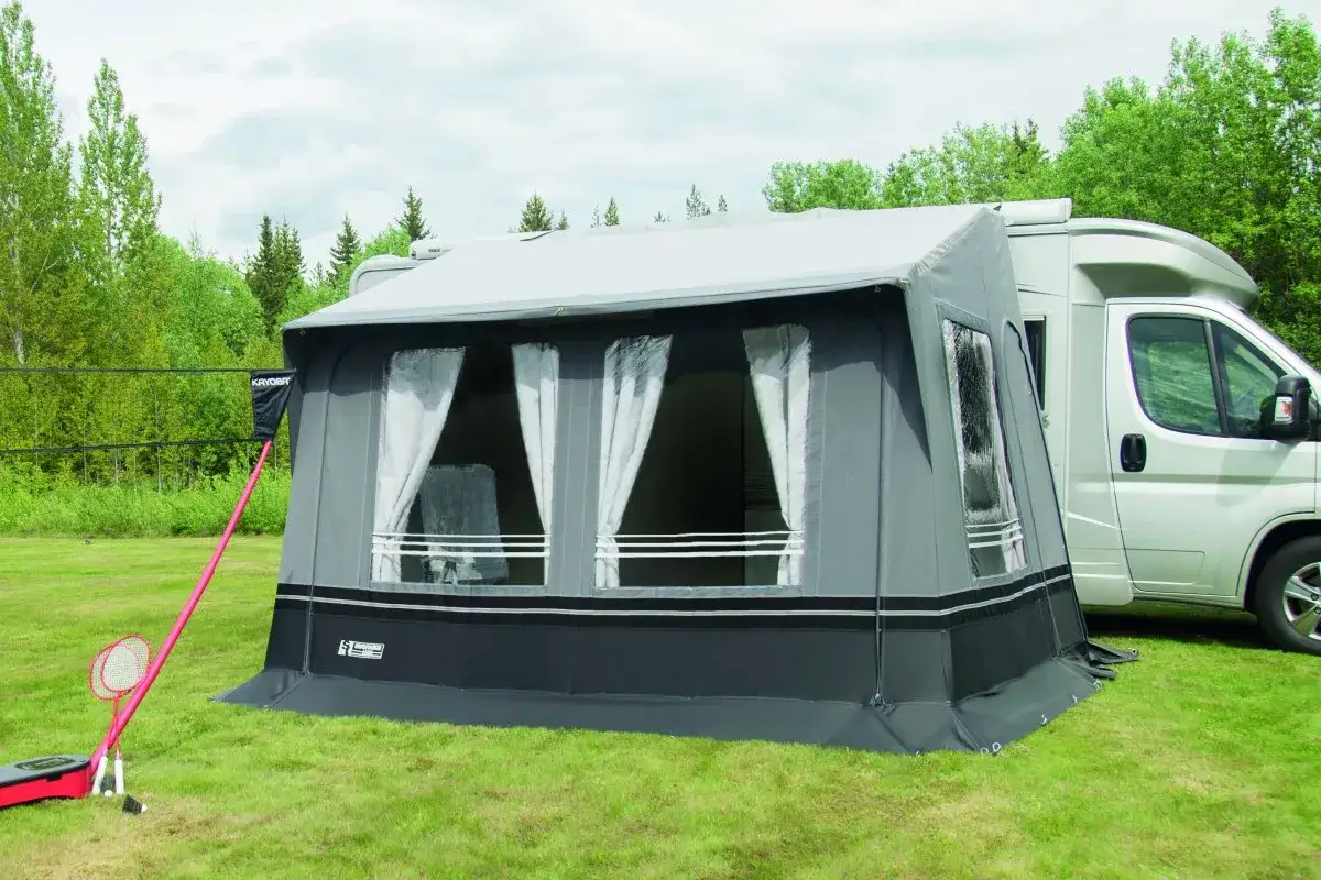 Förtält till husbilen, perfekt för billiga campingar. Soligt och grönt, med badmintonracketar redo för lek.
