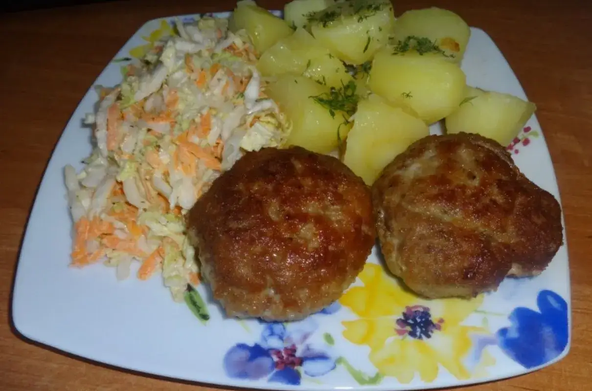 Dwa apetyczne kotlety mielone z piekarnika, podane z ziemniakami i surówką z kapusty i marchewki.