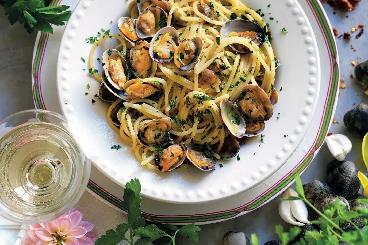 Spaghetti alle vongole, un classico abbinamento cibo vino, guarniti con prezzemolo fresco e accompagnati da un bicchiere di vino bianco.