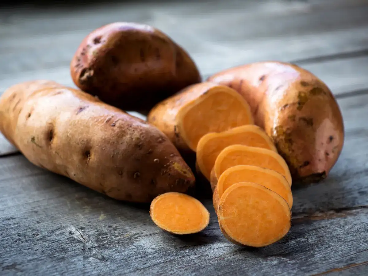Plusieurs patates douces, entières et coupées en rondelles, sur une table en bois.