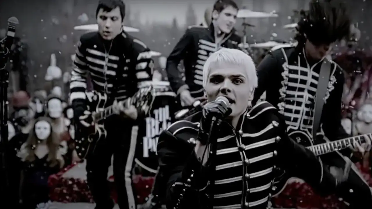 Zespół emo w mundurach gra na scenie, wokalista z blond włosami śpiewa do mikrofonu, tłum wpatrzony w nich.