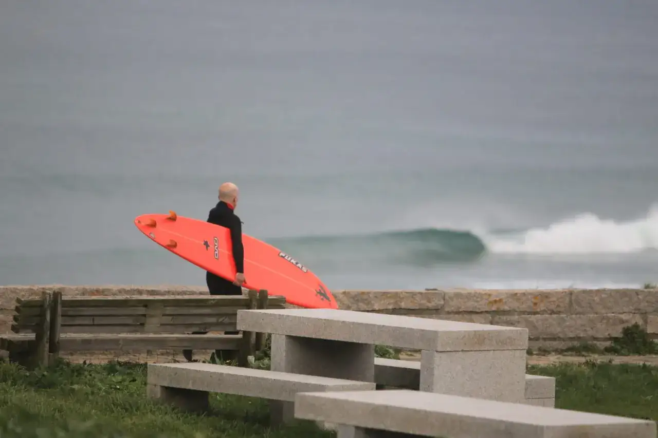 Hombre con tabla de surf naranja en la playa Longara Barreiros, listo para surfear las olas.
