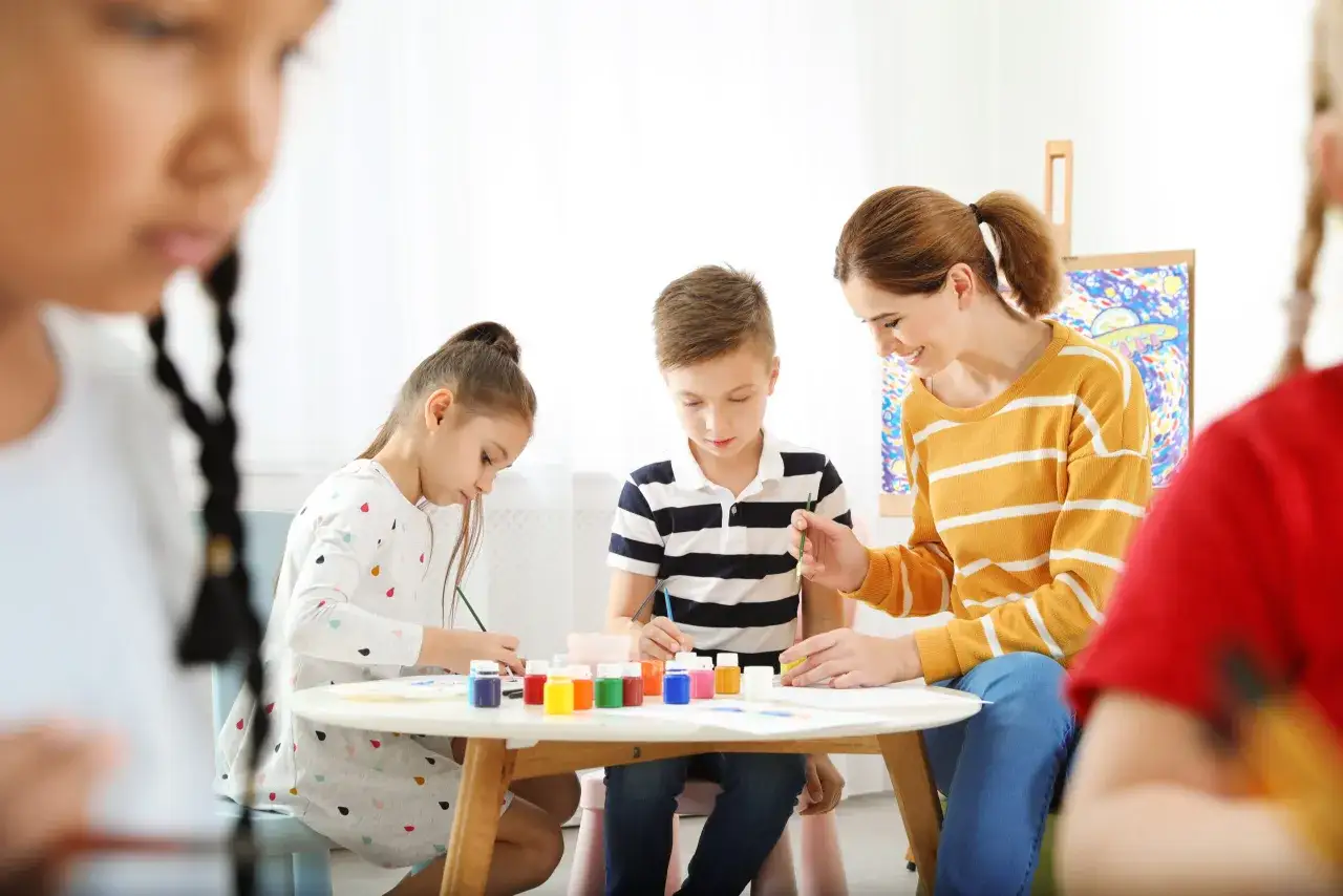 Niños pintando con su maestra en un taller creativo. Celebrando el día de la mujer para niños con arte y sonrisas.