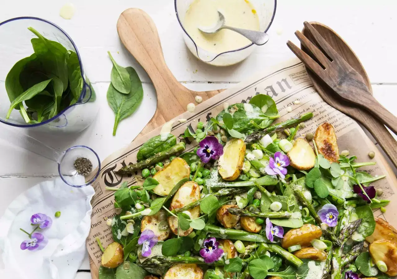 En härlig sallad med sparris, gröna ärtor, spenat och gyllene, rostad potatis, dekorerad med violer.