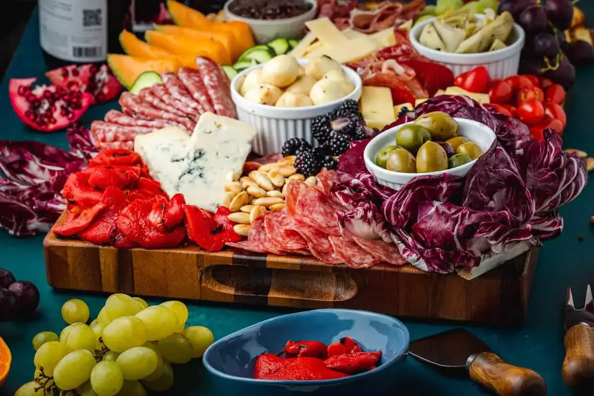 Eine üppige Platte mit Antipasti-Rezepten: Wurst, Käse, Oliven, Früchte und geröstete Paprika laden zum Genießen ein.