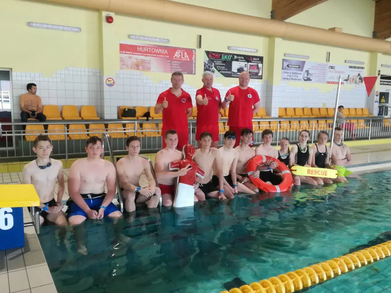 Grupa młodych ludzi w czerwonych koszulkach, gotowa do nauki, jak zostać ratownikiem wodnym.