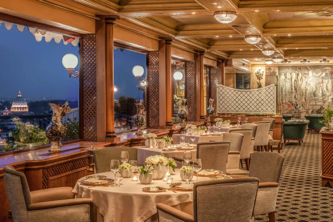 Tavoli apparecchiati in un elegante ristorante 3 stelle Michelin, con vista panoramica su Roma al tramonto.