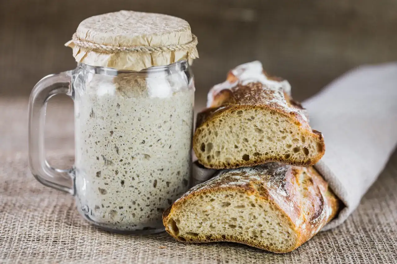 Un bocal de levain p&eacute;tillant &agrave; c&ocirc;t&eacute; de pains artisanaux coup&eacute;s. L'art de remplacer la levure par levain pour un go&ucirc;t authentique.