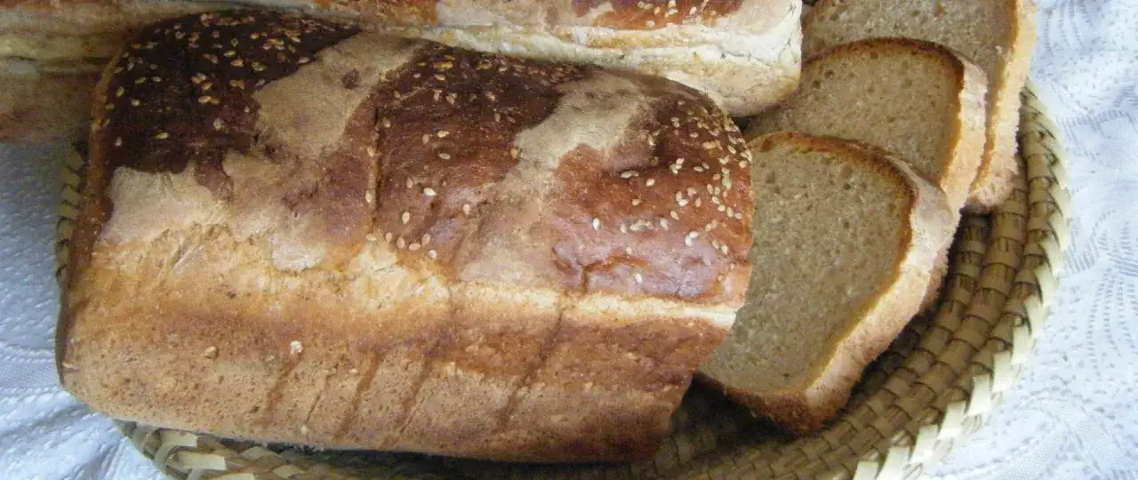 Chleb żytni z sezamem, pokrojony w kromki, leży w wiklinowym koszyku.