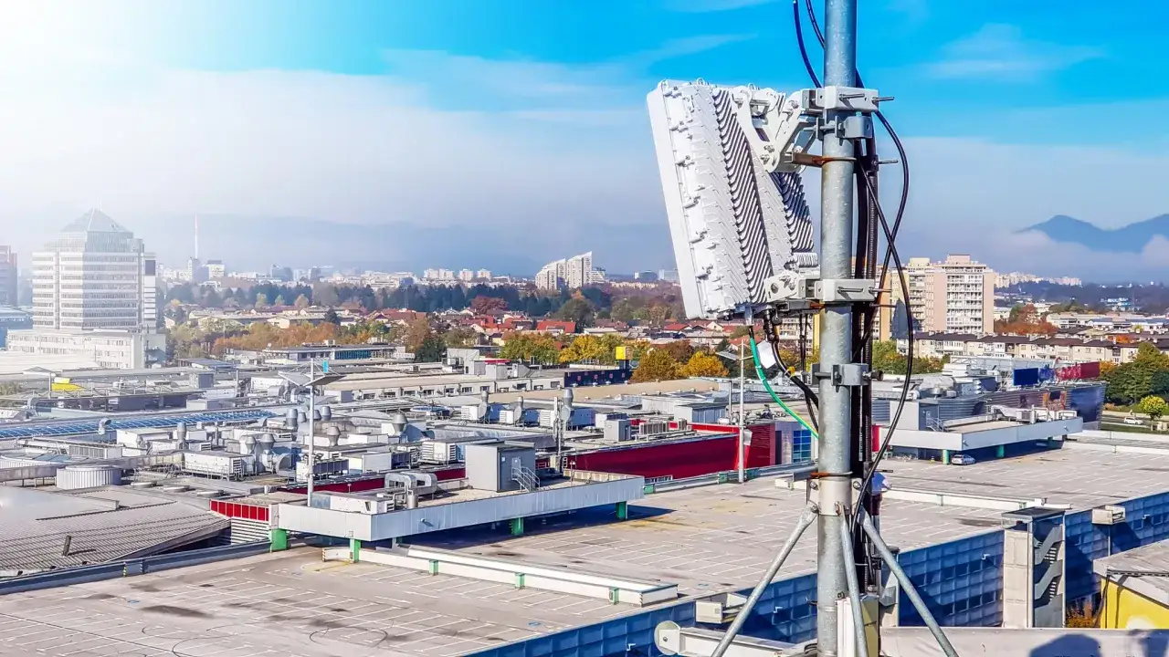 Antena de telefon&iacute;a m&oacute;vil emitiendo ondas milim&eacute;tricas sobre un paisaje urbano con edificios y monta&ntilde;as al fondo.