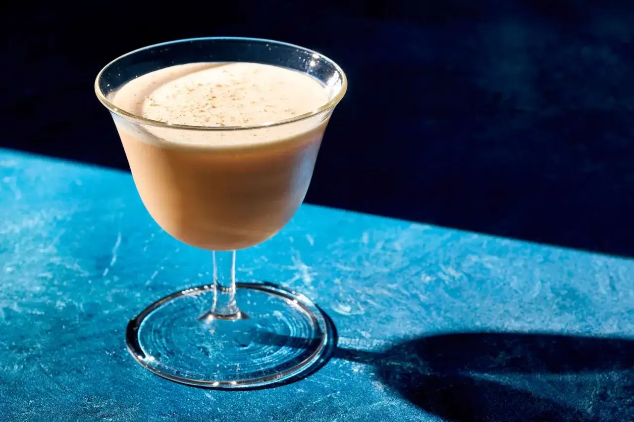 Cremiger Cocktail mit Eigelb, garniert mit etwas Zimt, auf blauem Untergrund.