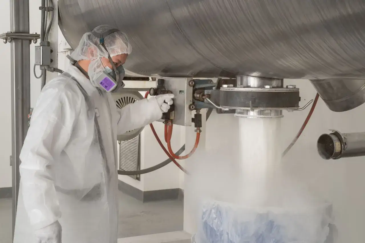 Mitarbeiter in Schutzkleidung &uuml;berwacht die Abf&uuml;llung von Pulver. Dies zeigt, wie wird proteinpulver hergestellt, in einer industriellen Anlage.