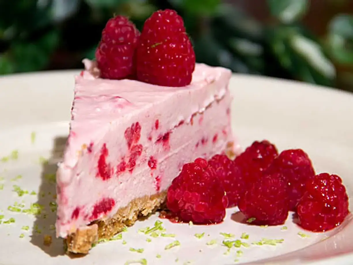 En bit kr&auml;mig, fryst cheesecake med hallon och f&auml;rska hallon som dekoration.