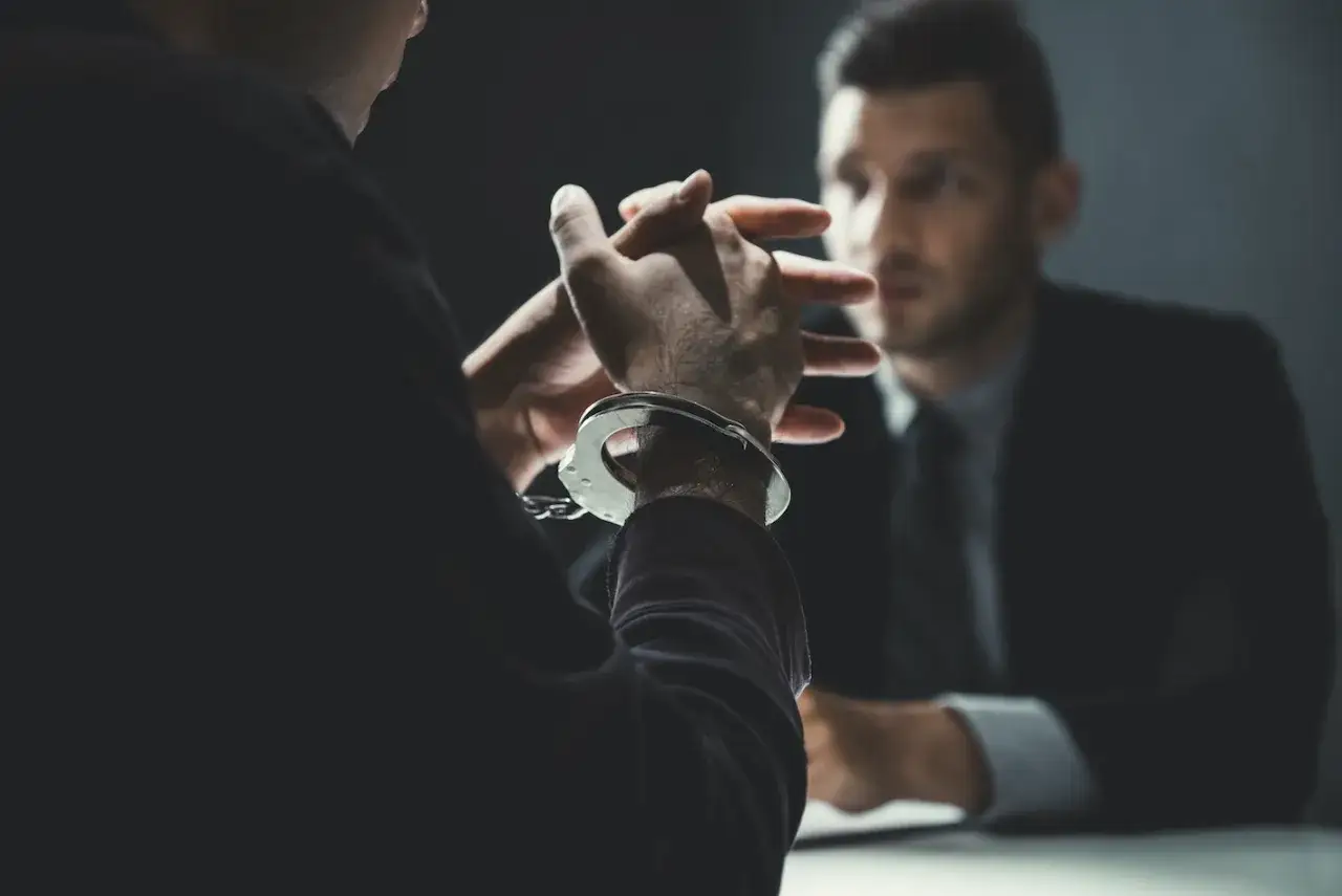 Dłoń w kajdankach, rozmowa z mężczyzną w garniturze.