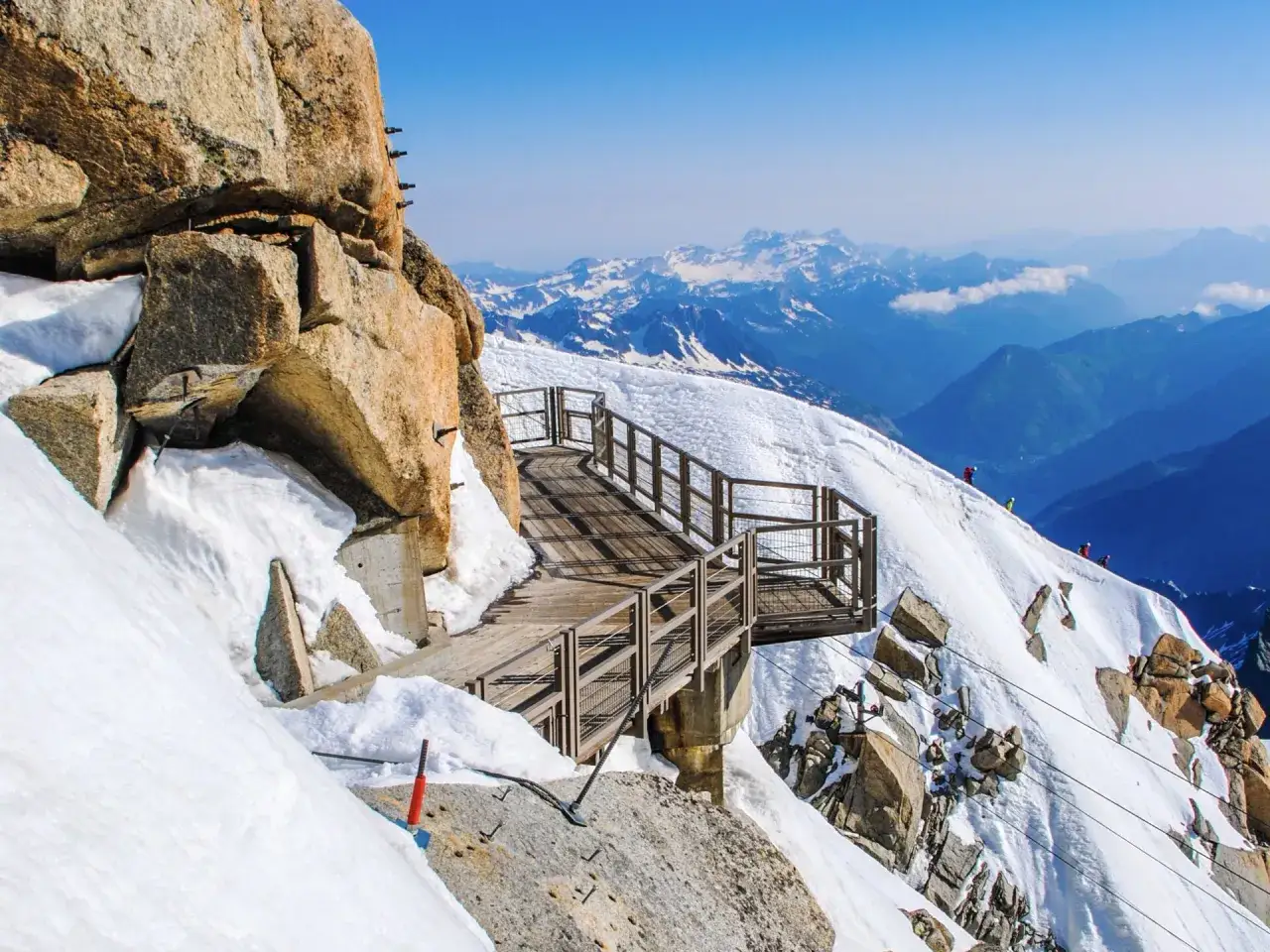 Holzsteg f&uuml;hrt &uuml;ber schneebedeckte Felsen, mit Bergsteigern, die den Mont Blanc besteigen.