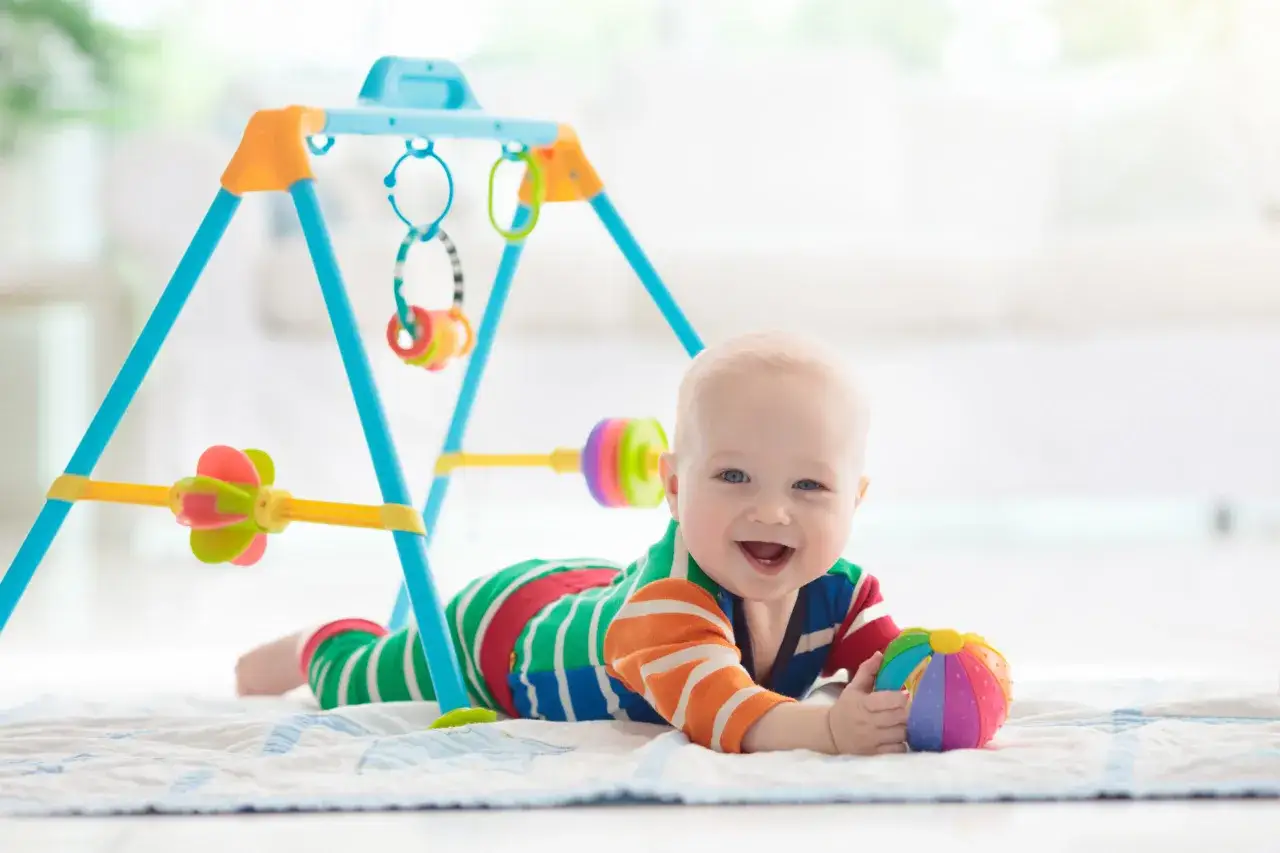 Ein fr&ouml;hliches Baby mit 6 Monaten liegt auf einer Decke und spielt mit einem bunten Ball. Es erkundet die Welt und was ein Baby mit 6 Monaten alles kann.
