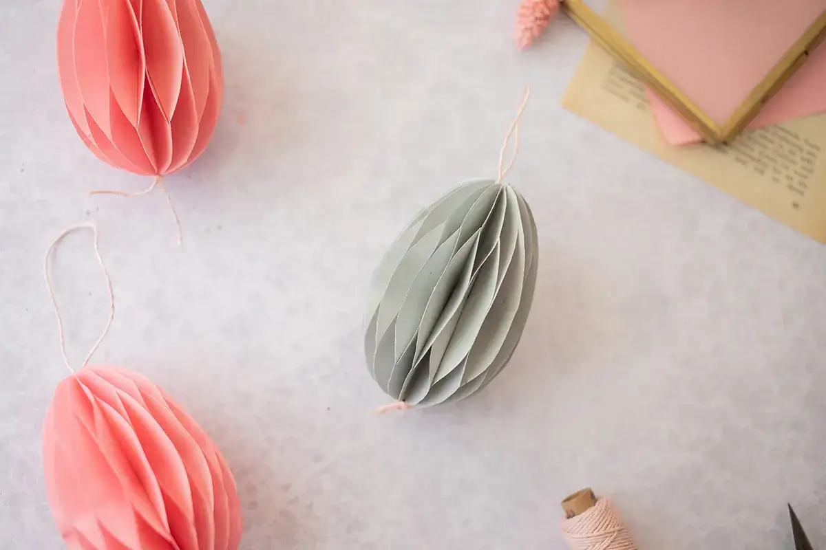 Ostereier basteln Papier: Dekorative Papier-Eier in Rosa und Grau, bereit zum Aufhängen.