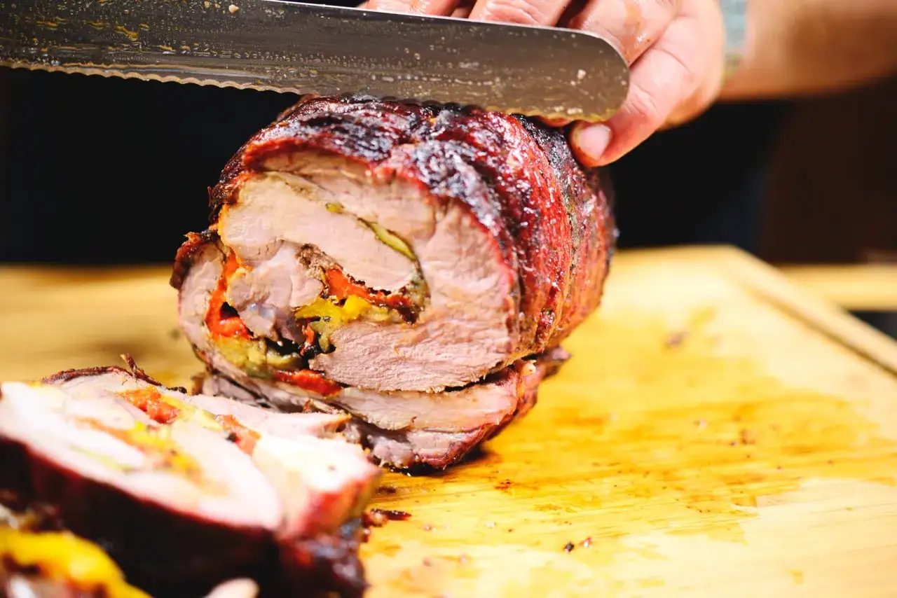 Coppa di maiale allo spiedo succulenta, ripiena e affettata su un tagliere di legno.
