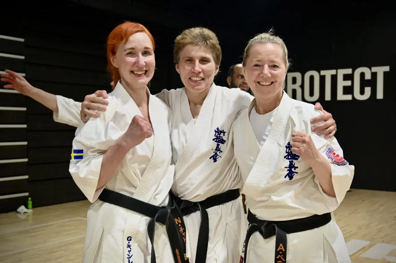 Tre glada kvinnor i vita karate-gi med svarta kyokushin karate bälten. En har svensk flagga på ärmen.
