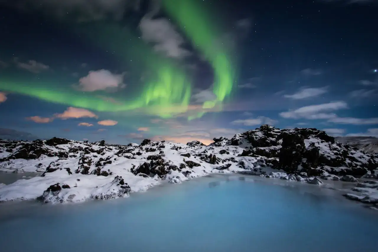 Vinterlandskap på en island med turkost vatten och snötäckta klippor under ett magiskt norrsken.