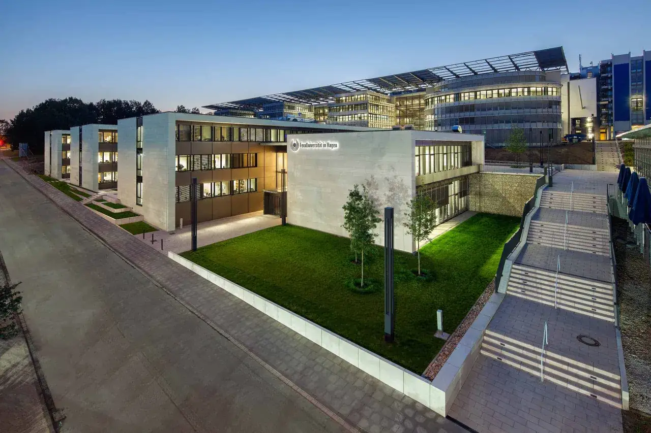 Moderne Geb&auml;ude der Fernuni NRW in Hagen bei D&auml;mmerung. Ein gepflegter Rasen und eine breite Treppe f&uuml;hren zum Eingang.