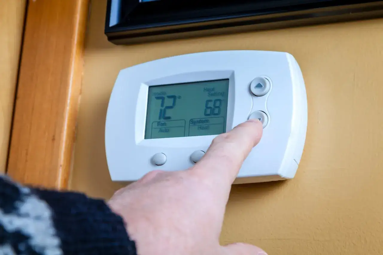 Dedo ajustando la altura del termostato. Muestra 72°F interior y 68°F de ajuste de calor.