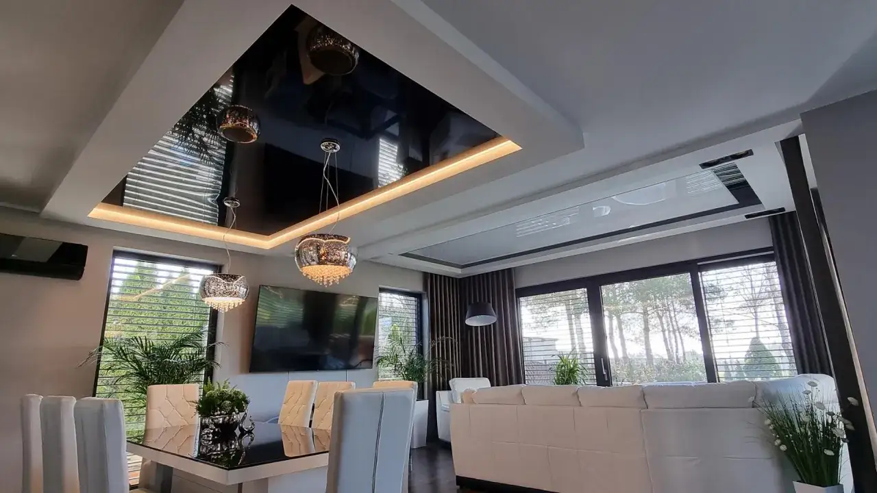 Nowoczesny salon z błyszczącym, czarnym sufitem napinanym lustrzanym, kt&oacute;ry odbija eleganckie lampy i okna.