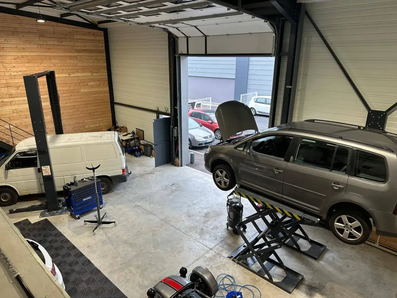 Un garage électronique auto avec une voiture sur un pont élévateur, un fourgon blanc et d'autres véhicules à l'extérieur.