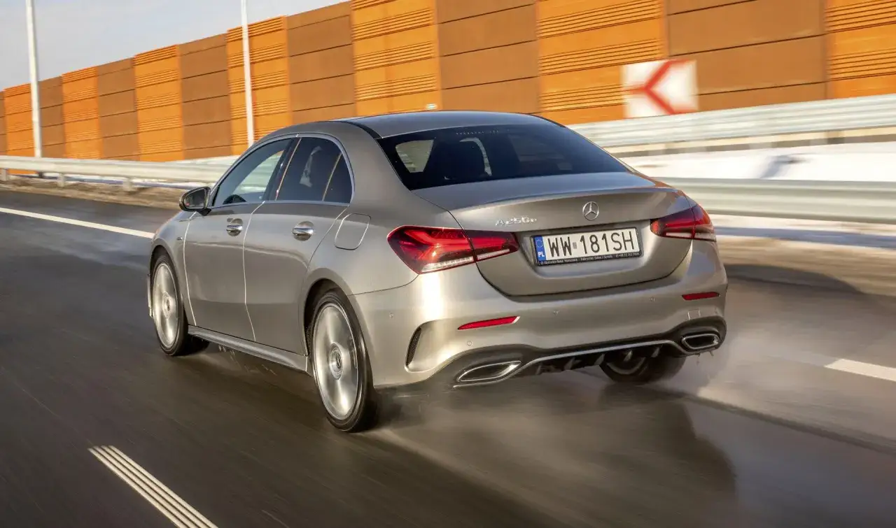Srebrny Mercedes-Benz W177 A250e pędzi po mokrej drodze, rozpryskując wodę.