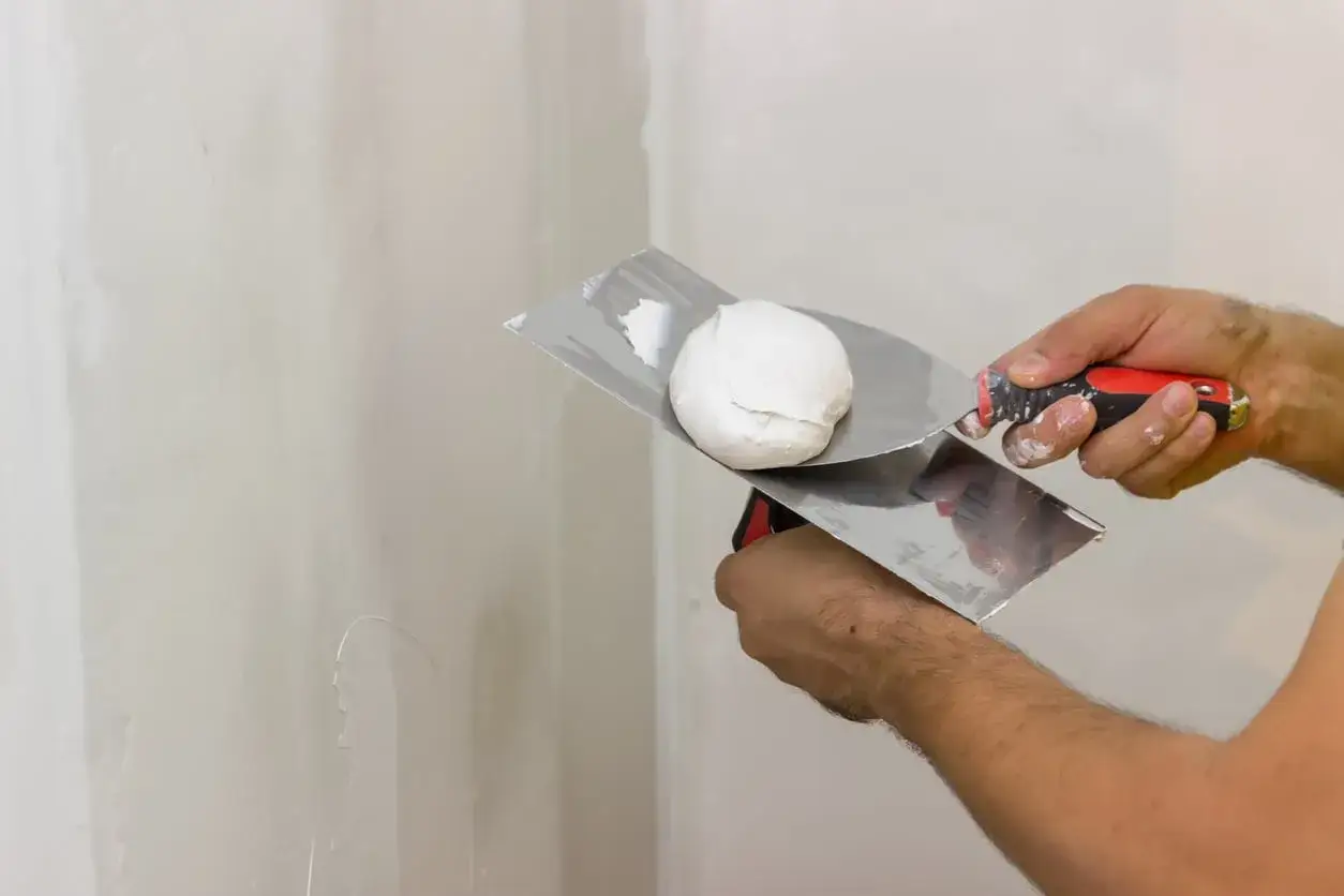 Mani che lavorano con spatole e stucco murale per preparare una parete.